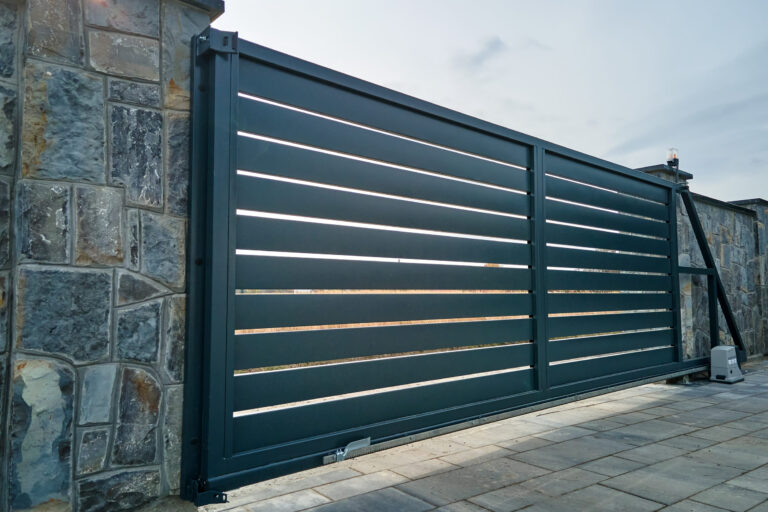 Wide automatic sliding gate with remote control installed in high stone fense wall. Security and protection concept